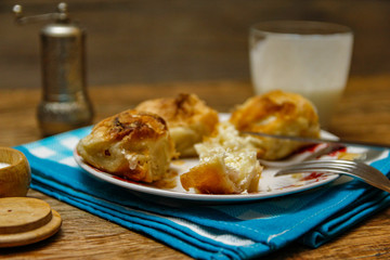 Traditional Bosnian pastry- manti borek with cheese on wooden table with yogurt. rustic background with low light and old bowls.