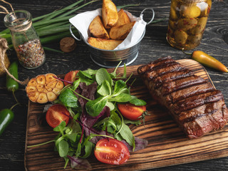 steak on the board with herbs, fried potatoes, spices on a black surface