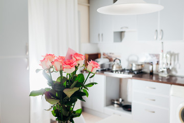 Bouquet of roses with card left on kitchen. Modern kitchen design. Interior of kitchen decorated with flowers.