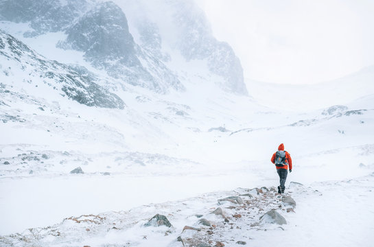 Climber walks alone in high mountains at windy snowy weather