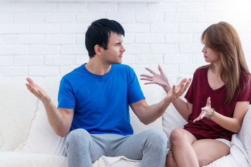 Unhappy couples at home. Handsome man and beautiful young woman are sitting on white sofa together....