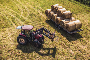 Aerial Drone Photo of Farmer Harvesting Hay Rolls in the Wheat Field with a Red Tractor
