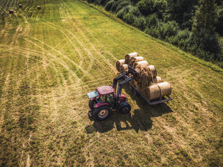 Obraz premium Aerial Drone Photo of Farmer Harvesting Hay Rolls in the Wheat Field with a Red Tractor
