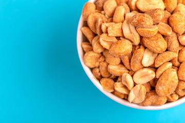 Roasted peanuts in paper cup on bright blue background