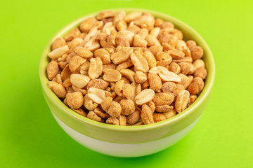 Roasted peanuts in bowl on bright green background