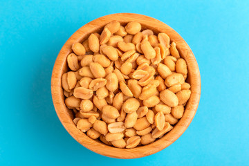 Roasted peanuts in wooden bowl on bright blue background