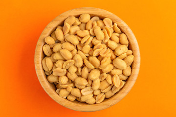 Roasted peanuts in wooden bowl on bright orange background