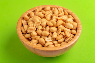 Roasted peanuts in wooden bowl on bright green background