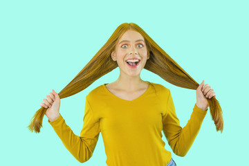 Joyful carefree girl with beautiful red long hair holding hair in both hands smiles...