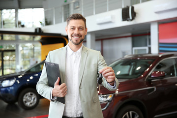 Salesman with clipboard and car keys in modern auto dealership