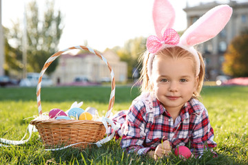 Cute little girl with bunny ears and basket of Easter eggs in park