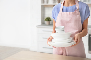 Woman with clean dishes and cups in kitchen, closeup. Space for text