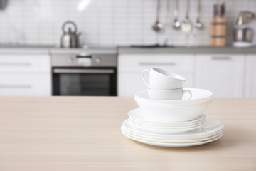 Stack of clean dishes and cups on table against blurred background. Space for text