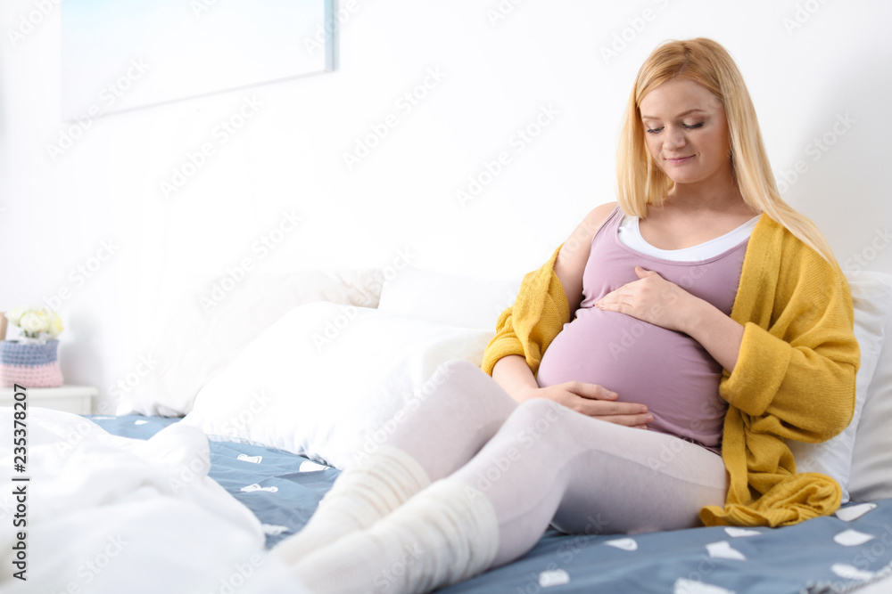 Poster beautiful pregnant woman resting on bed in light room. space for text