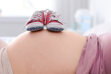 Pregnant woman with baby booties on blurred background, closeup view