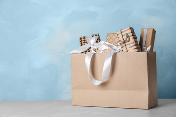 Paper shopping bag with handles full of gift boxes on table. Mock up for design
