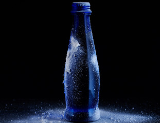 Blue glass bottle on a black background with snow and spruce branches