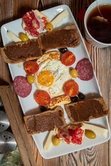 Breakfast with fried egg, rye bread, pomegranate, carob paste, cheeses, olives, dry salami, tomatoes and tea