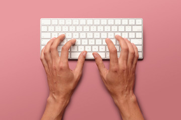 Flat lay with hands typing on white key board on pink table