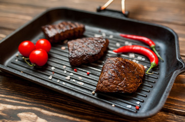 steaks, roast beef in a frying pan with spices, tomatoes, chili pepper, on wooden background, top view