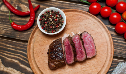 steaks, roast beef on the board with spices, tomatoes, chili pepper, on wooden background, top view