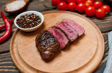 steaks, roast beef on the board with spices, tomatoes, chili pepper, on wooden background, top view