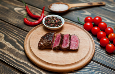 steaks, roast beef on the board with spices, tomatoes, chili pepper, on wooden background, top view