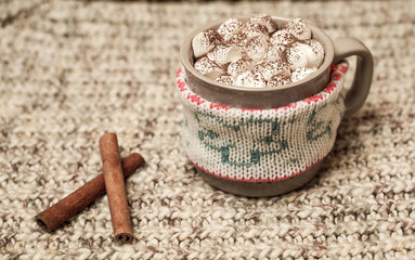 Fototapeta na wymiar Cappuccino with marshmallows in a mug on a woolen scarf