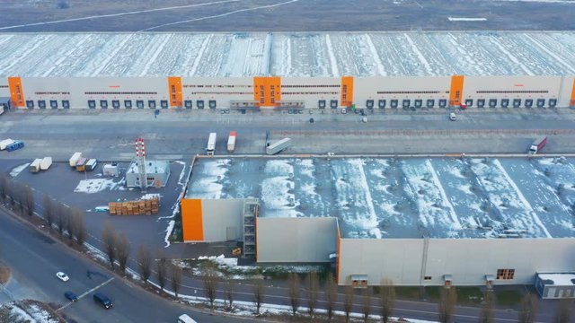 Aerial side view of the big warehouse logistics park with a semi-trailer trucks 
