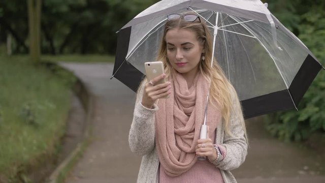 Young beautiful blonde model checking social networks on smartphone to stay connected outside of the city cloudy rainy day