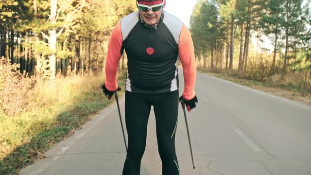 Training an athlete on the roller skaters. Biathlon ride on the roller skis with ski poles, in the helmet. Autumn workout. Roller sport. Adult man riding on skates. Shooting an athlete in motion