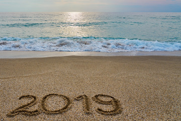 New year 2019 inscription  written on the sand with waving sea on a sunset. Copy space. 