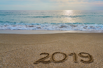 New year 2019 inscription  written on the sand with waving sea on a sunset. Copy space. 