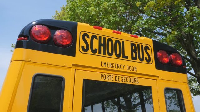 Back of Canadian schoolbus. English and French language on back door. Green leaves in the background.