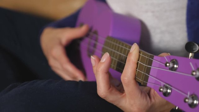 Detail of caucasian woman's hand playing purple ukelele. Fret hand in focus.