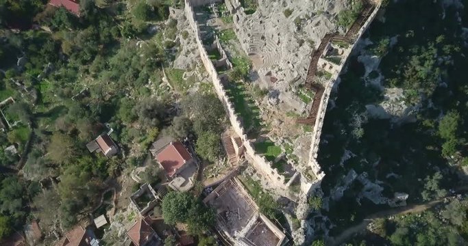 Reverse aerial drone video reveal of Simena Castle ruins above Kalekoy village and shallow turquoise coast of Mediterranean Sea near Kekova Island, Turkey. 4k at 23.97fps