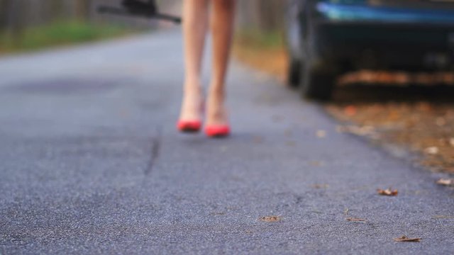 4K. Sexy womans legs in red  high-heeled shoes and car trouble, woman puts emergency sign