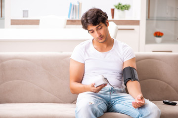 Fototapeta premium Young man measuring blood pressure at home