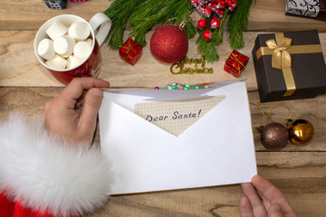 Santa Claus received a letter and holds it in his hands at the North Pole in Lapland, male hands on a wooden background with decorations and Christmas gifts.