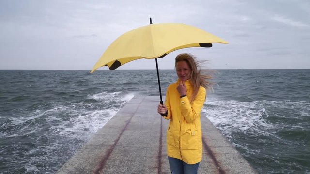 Girl in yellow rain cover with yellow umbrella at sea pier rainy day slow motion