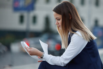 Pretty cheerful young blonde girl in smart casual eclectic outfit sits on cafe terrace while drinking coffee from paper cup. Coffee to go