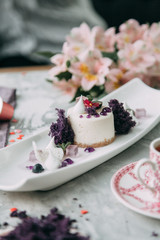 Dessert with flowers and coffee on the table. Foodstyling with decor and sweets in purple.