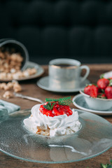 Pavlova dessert with berries in a beautiful composition. Foodstyling on a wooden background with coffee and strawberries.