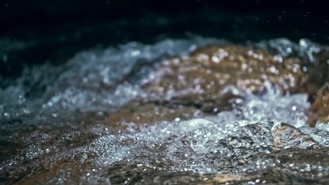 Slow motion of waves on dark water surface with play of flecks of bright light close up. Amazing dramatic natural background. Shooting with 180fps. Epic mystical and magic night view. Crystal clear
