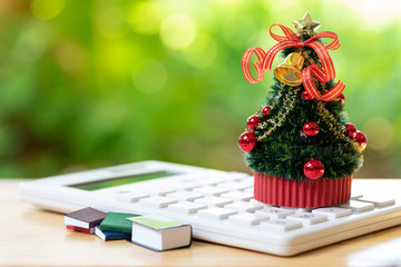 A beautifully decorated Christmas tree placed on a white calculator and with a miniature book....