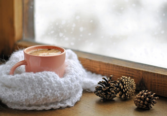Wooden winter window. A cup of hot coffee and a warm white knitted scarf on the windowsill. Still...
