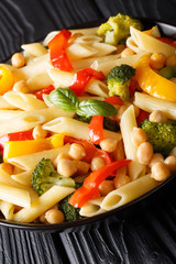 Delicious Italian penne pasta salad with chickpeas, broccoli, bell peppers closeup in a plate on the table. vertical
