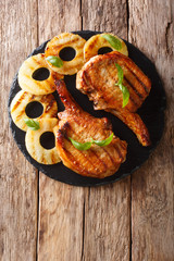 Main course: grilled pork chop steak in honey glaze with pineapples close-up on a slate plate....