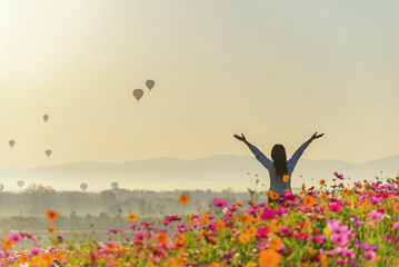 Lifestyle traveler women raise hand feeling good relax and happy freedom and see the fire balloon on the nature tea and cosmos farm in the sunrise morning. Travel and summer Concept - obrazy, fototapety, plakaty