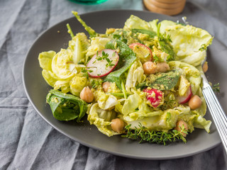 Plant based avocado spinach salad with chickpeas, lettuce and radish on gray table cloth